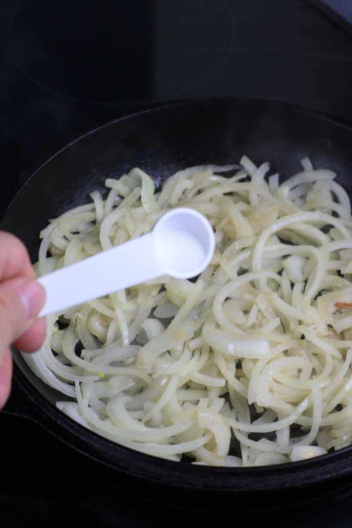 Adding salt to sliced onions in a pan.