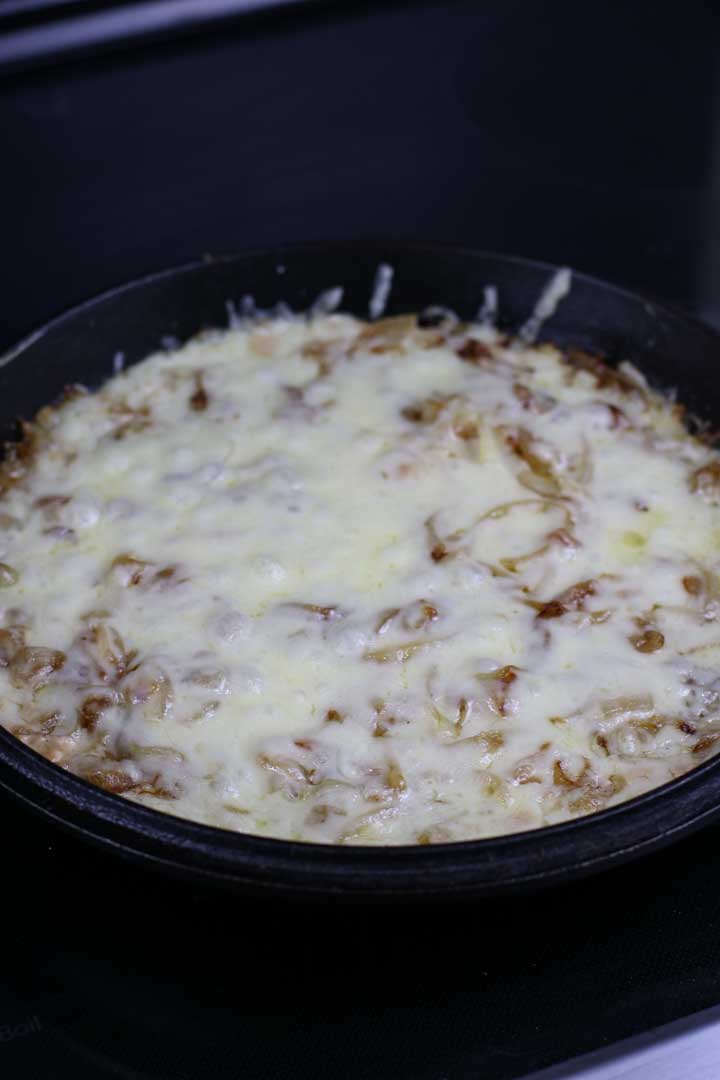 Cheese melted on onion dip in a cast iron pan.