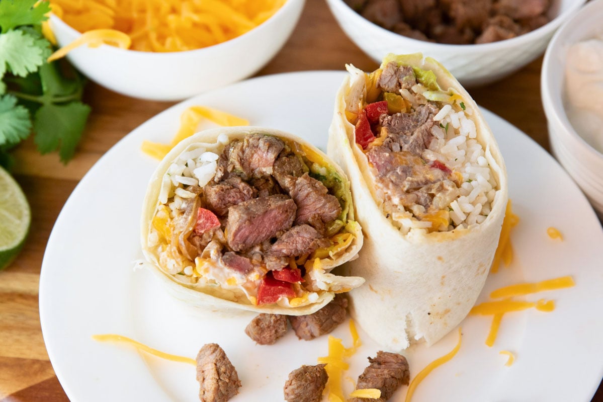 easy steak burrito on a plate. Bowls of toppings sitting in background