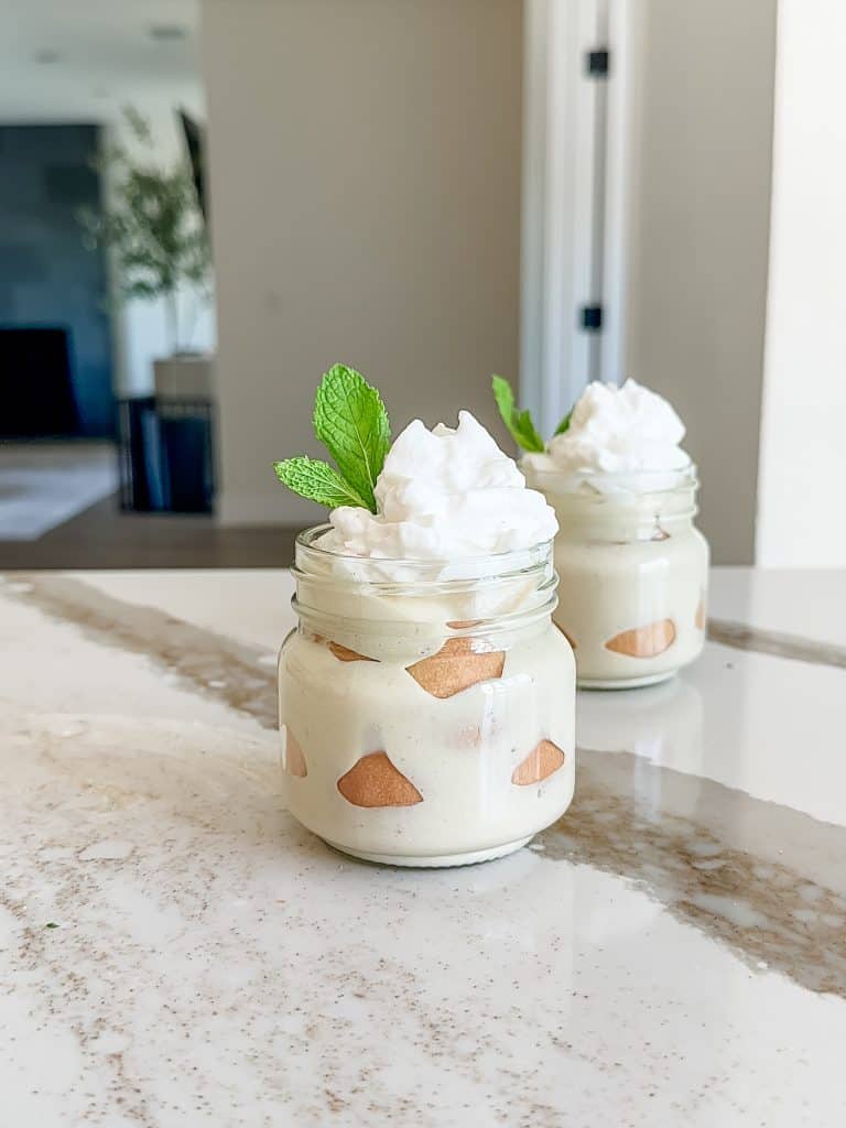 two banana puddings on a counter, in jars that are layered with vanilla wafers, pudding, banana and whipped cream