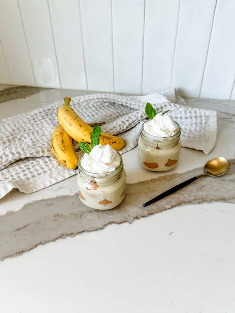 two jars of high protein banana pudding on the counter next to two ripe bananas 