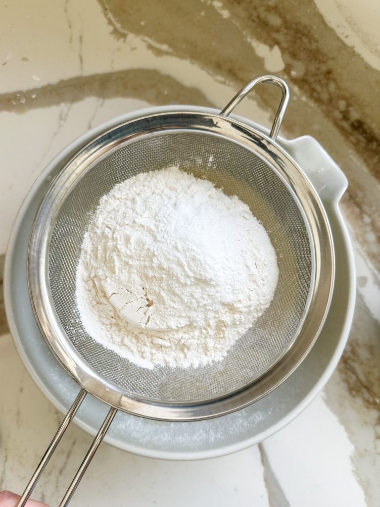 dry ingredients added to a sifter on top of the bowl