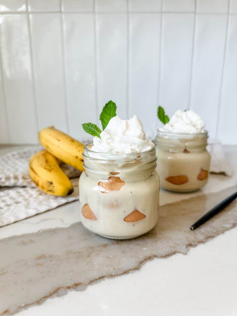 two banana puddings in jars that are topped with whipped cream and garnished with mint. 